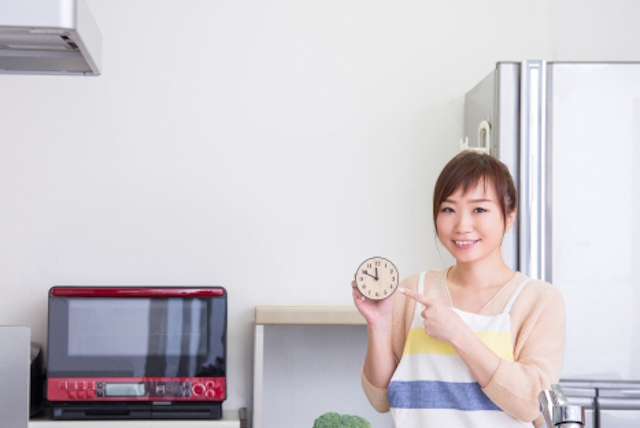 キッチンで時計を持つ笑顔の女性